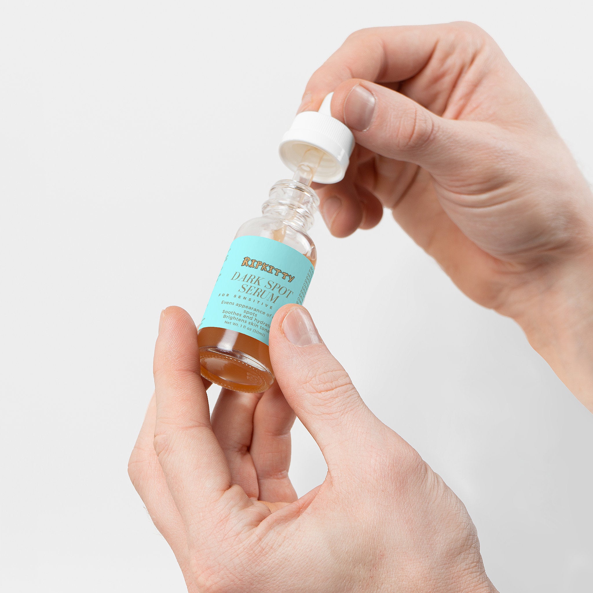 Hand holding a dropper bottle of serum with a light blue label against a white background