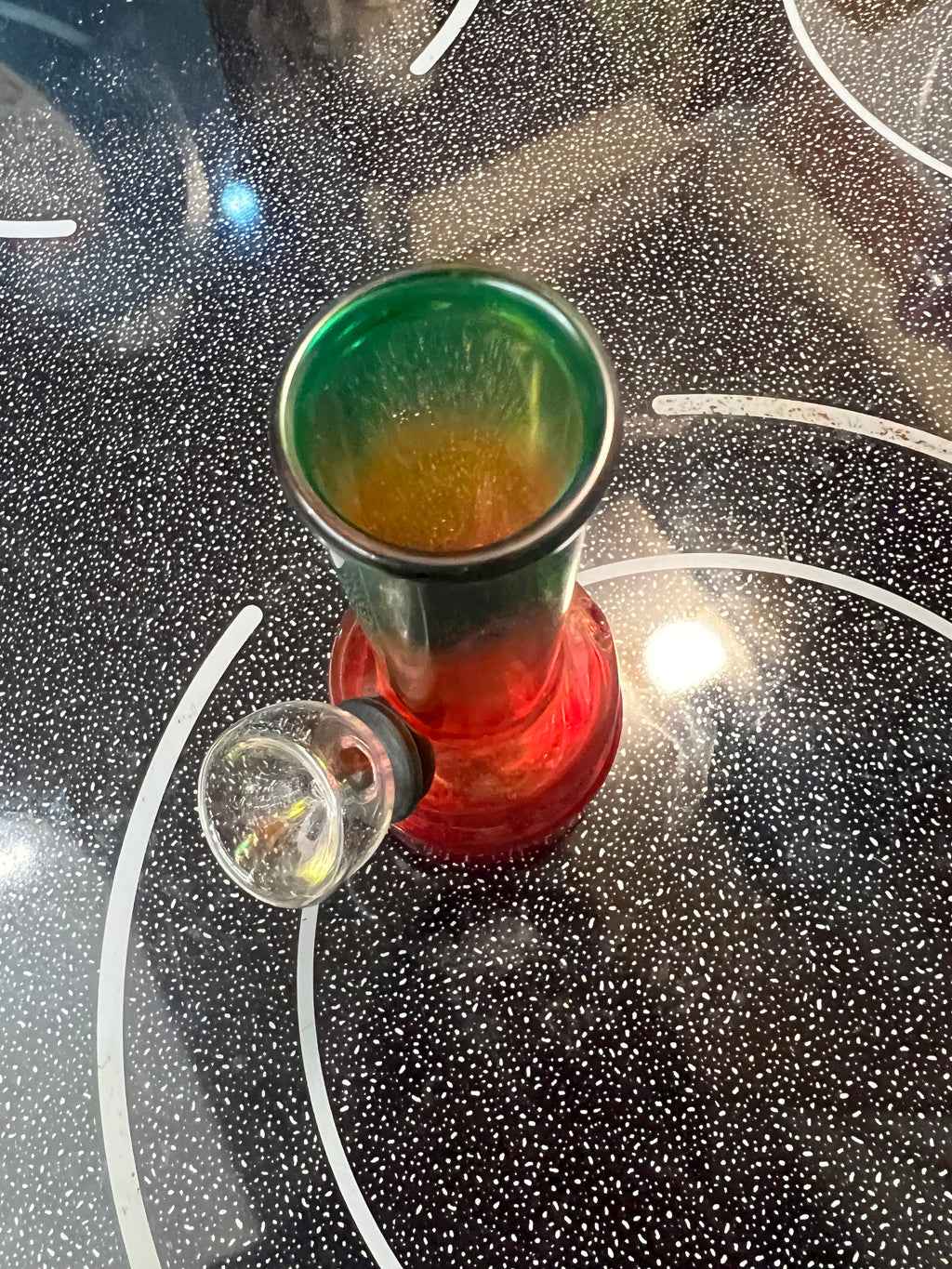Ripkitty 5-inch soft glass water pipe top-down view, red to green gradient colorway, bowl piece removed, shown on black stovetop surface