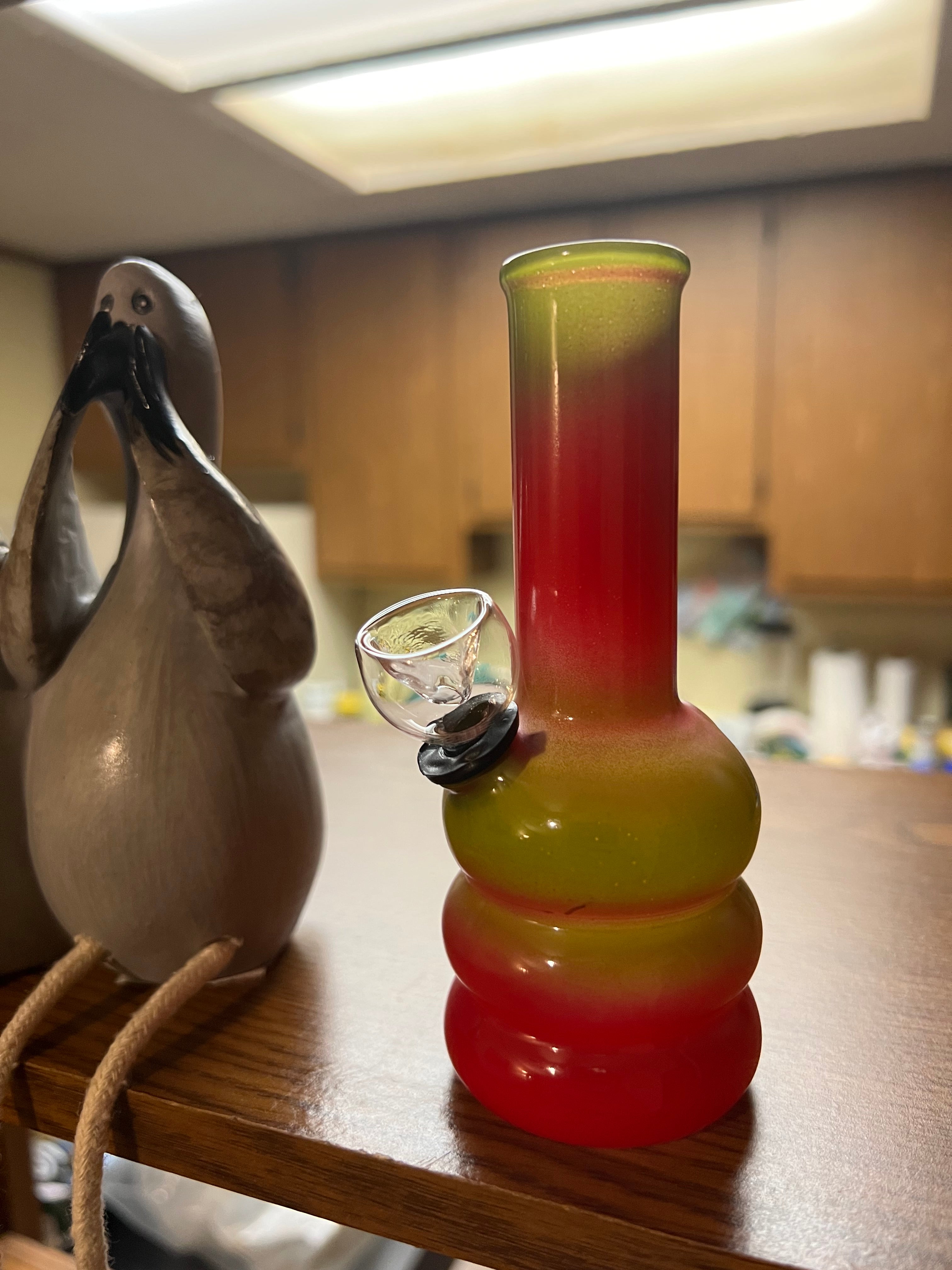 Ripkitty 5-inch soft glass water pipe, red to olive gradient colorway, full height view with triple-bubble base, clear bowl piece, decorative bird figurine beside it