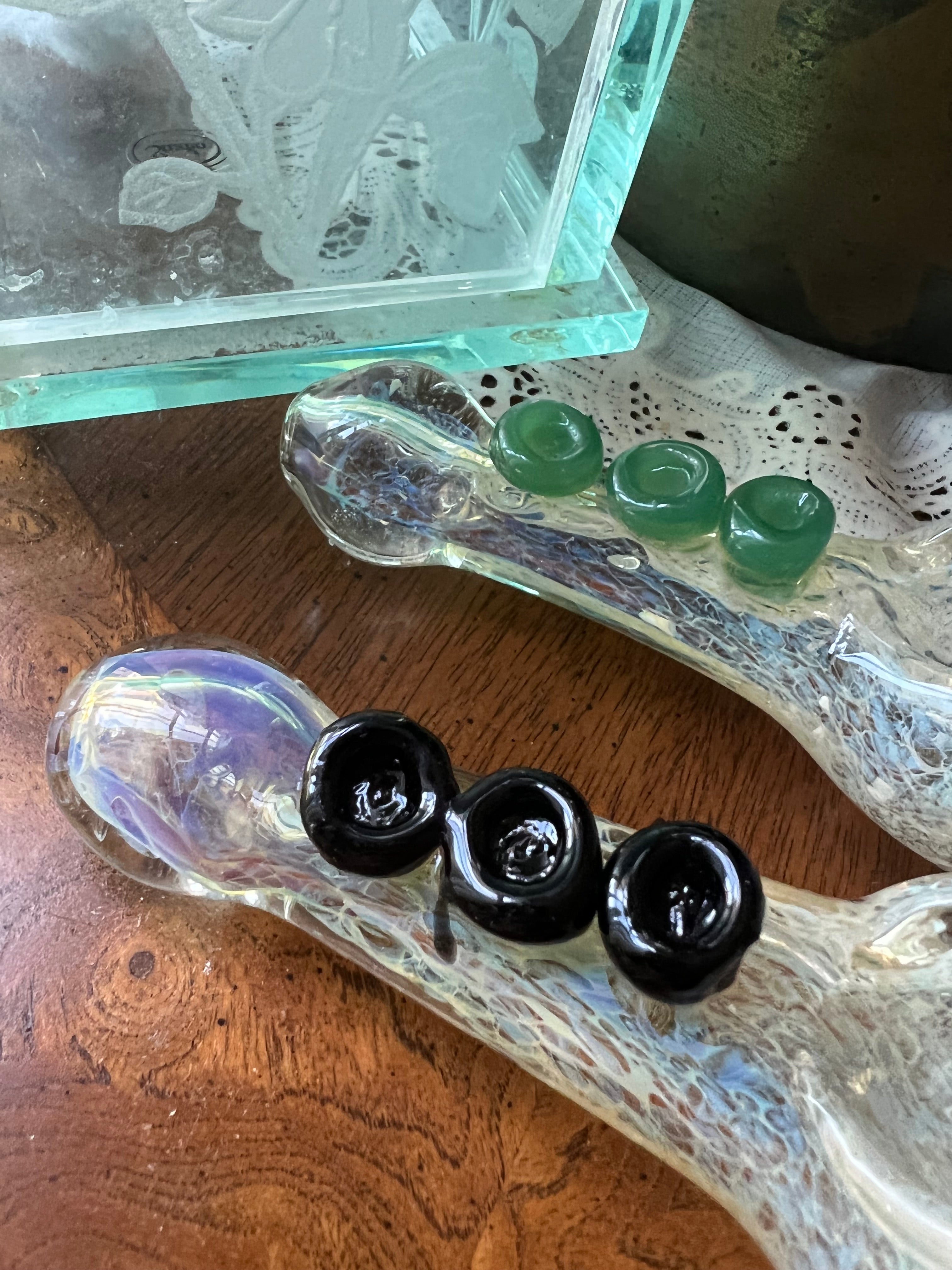Close-up of two Ripkitty silver fumed frit glass hand pipes showing green jade and black rose marble accent details on textured frit bodies