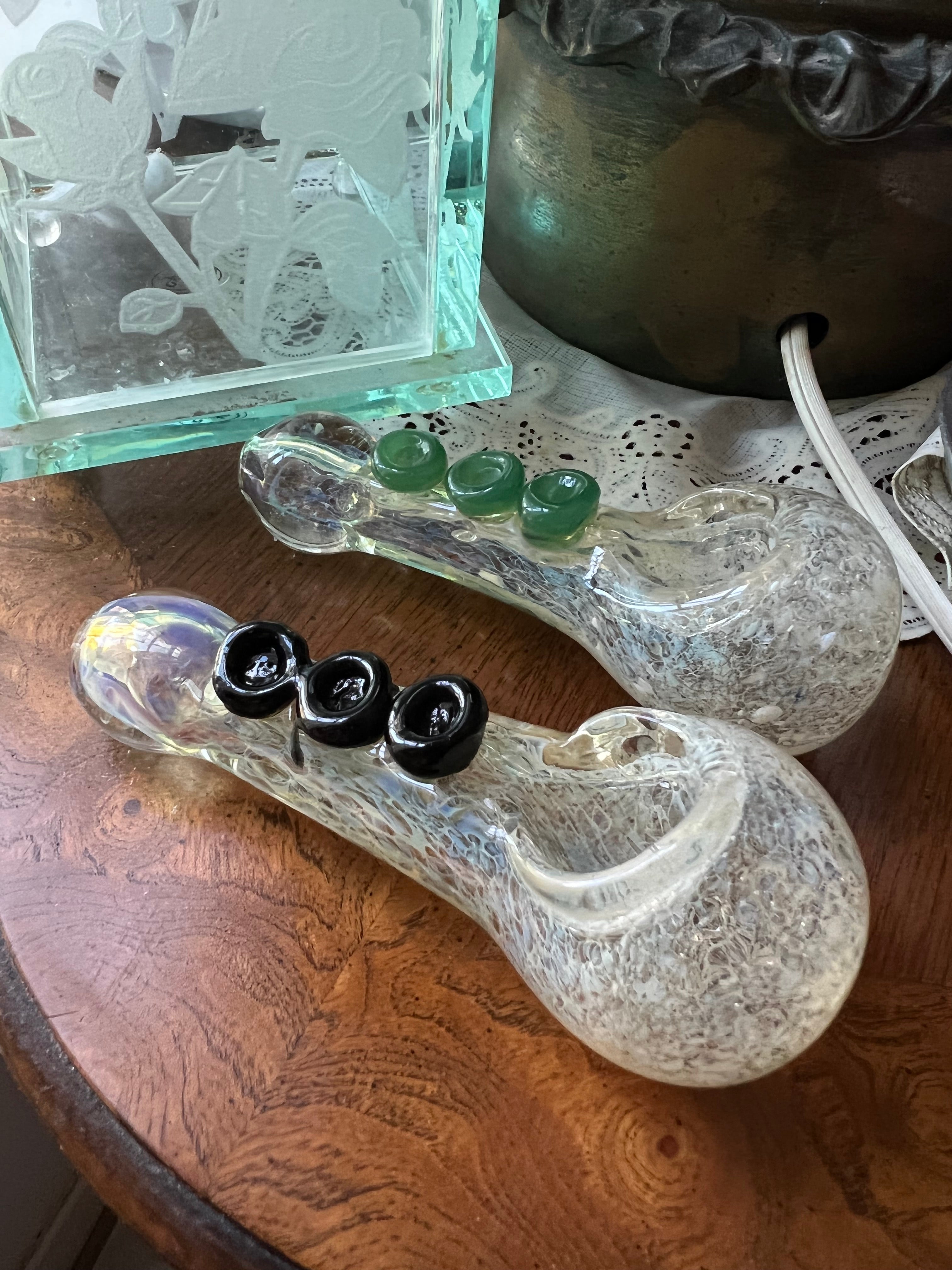 Two Ripkitty 4" silver fumed frit glass hand pipes side by side — one with green jade marble accents, one with black rose marble accents — displayed on a wood surface