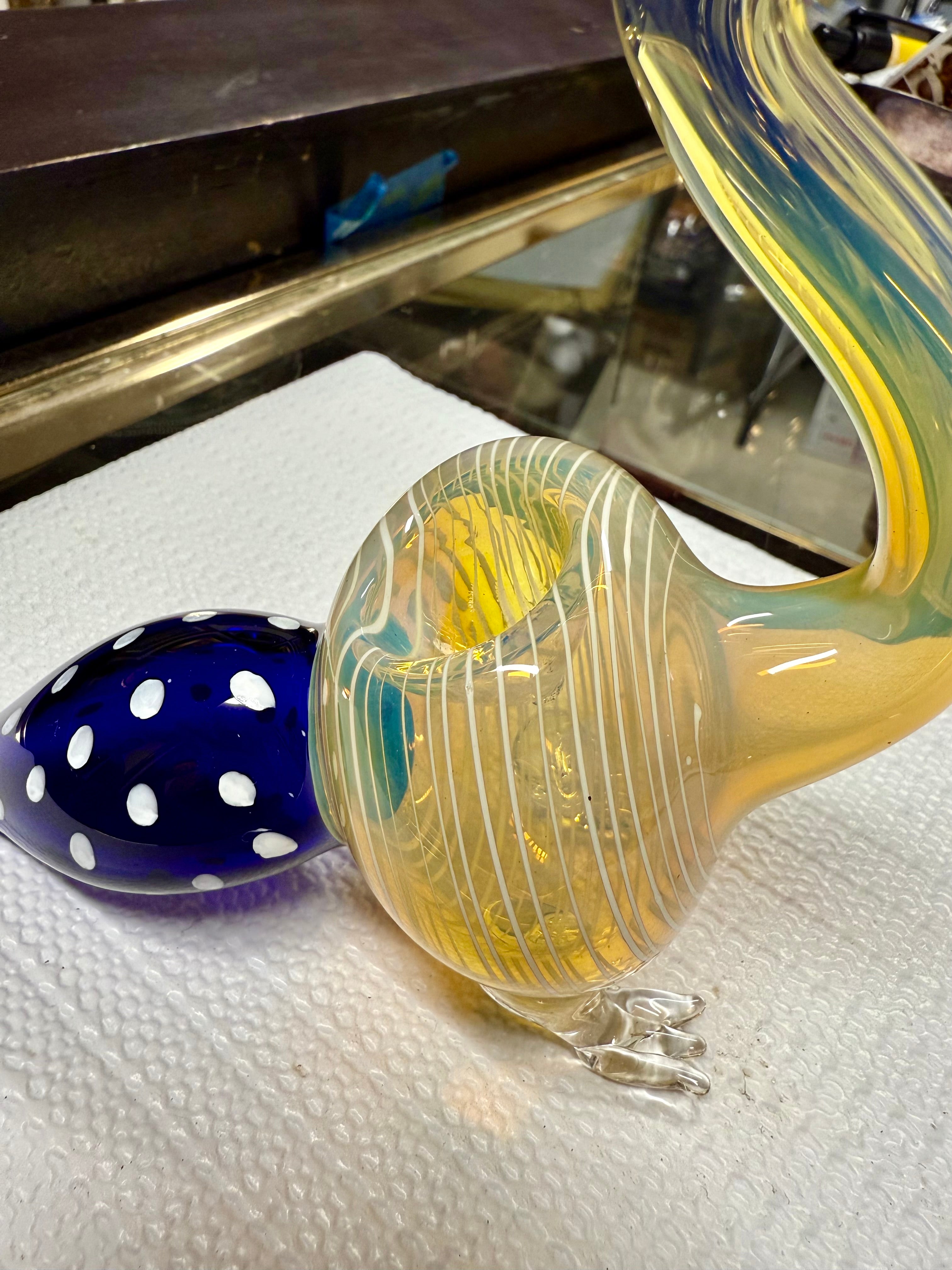 Close-up of Ripkitty peacock pipe mouthpiece — dark amber beak with crest prong accents and glass eye bead detail, teal-striped neck