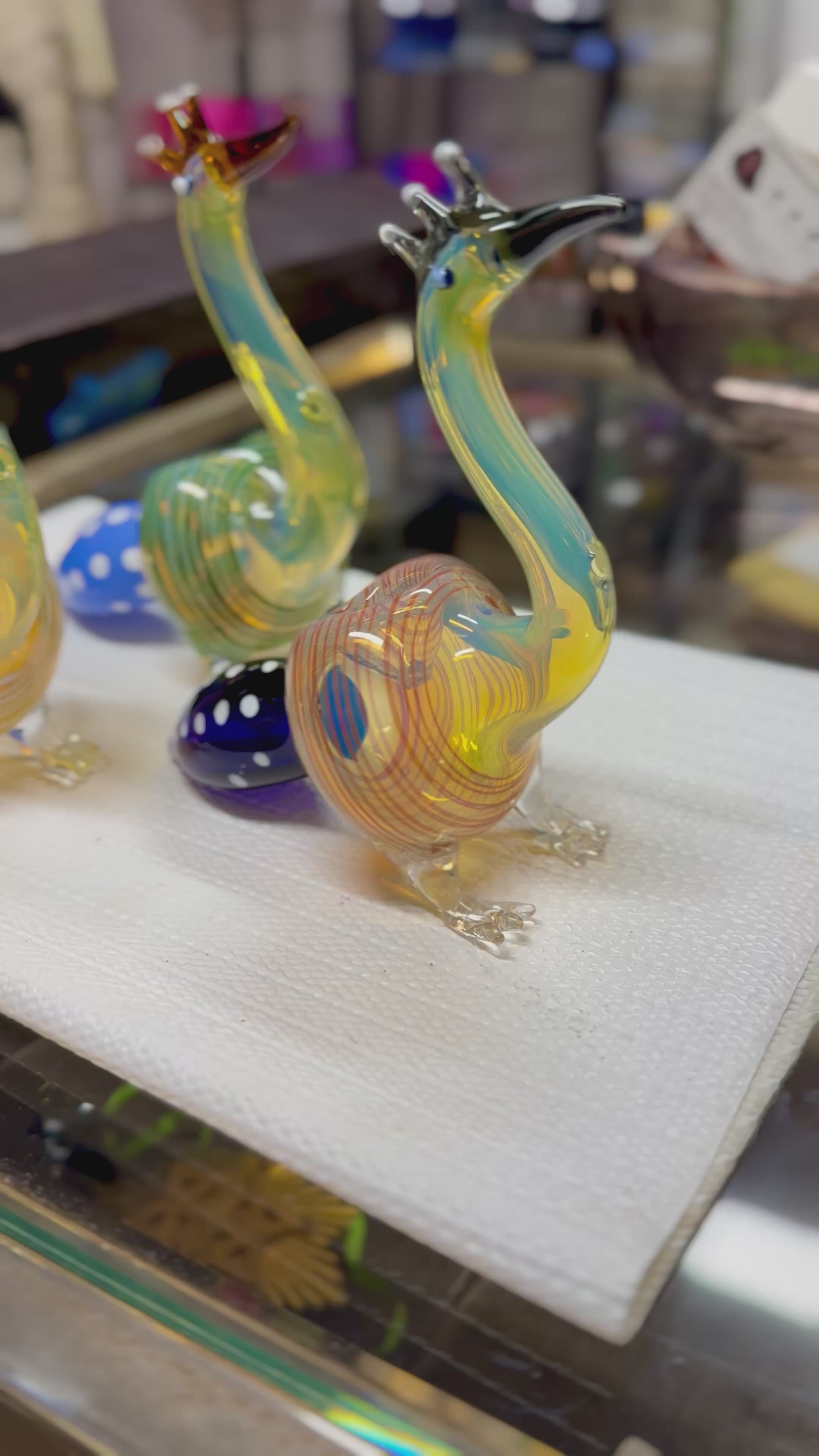 Ripkitty 5" peacock art borosilicate glass hand pipe — 360° display video showing sculpted peacock form, teal and amber-red colorways, crest prong mouthpiece, glass eye bead, and blue polka-dot bowl